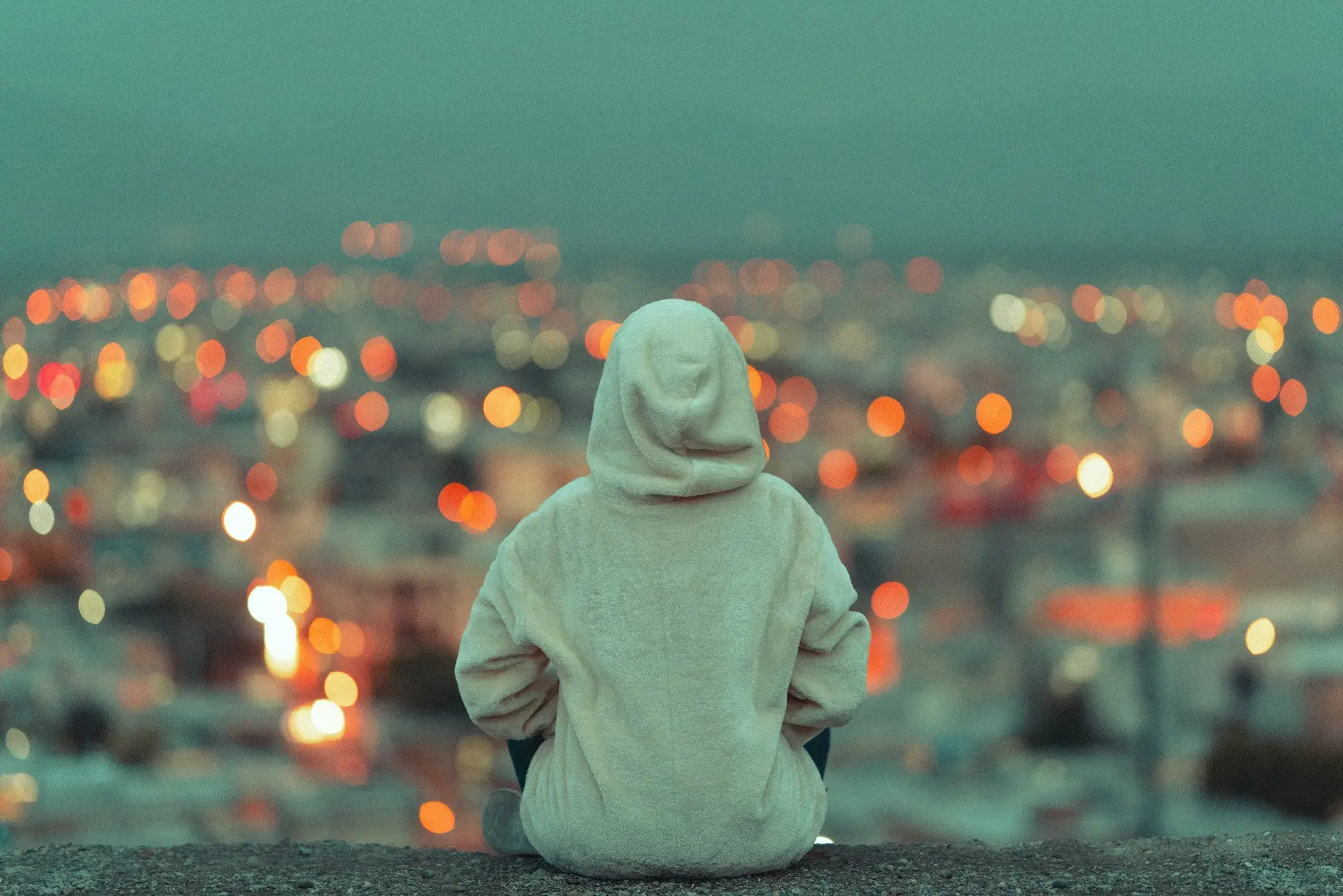 person in white hoodie sitting on gray concrete floor during daytime